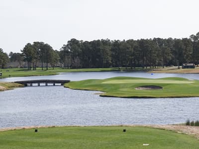 Early morning tee shot on a Myrtle Beach golf course, with fairway bunkers, pines, and a cart path curving toward the green.